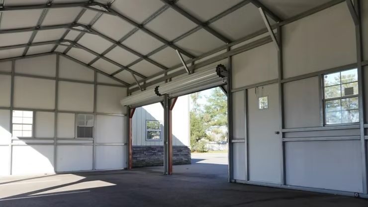 Interior of a metal framed structure with a large open doorway, white walls, and two windows.