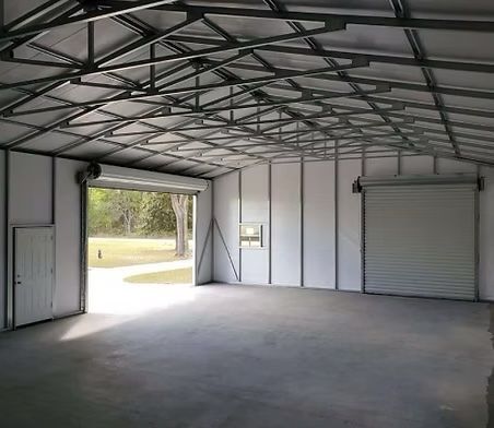 Interior of a metal building with roll-up doors, a concrete floor, and white walls.