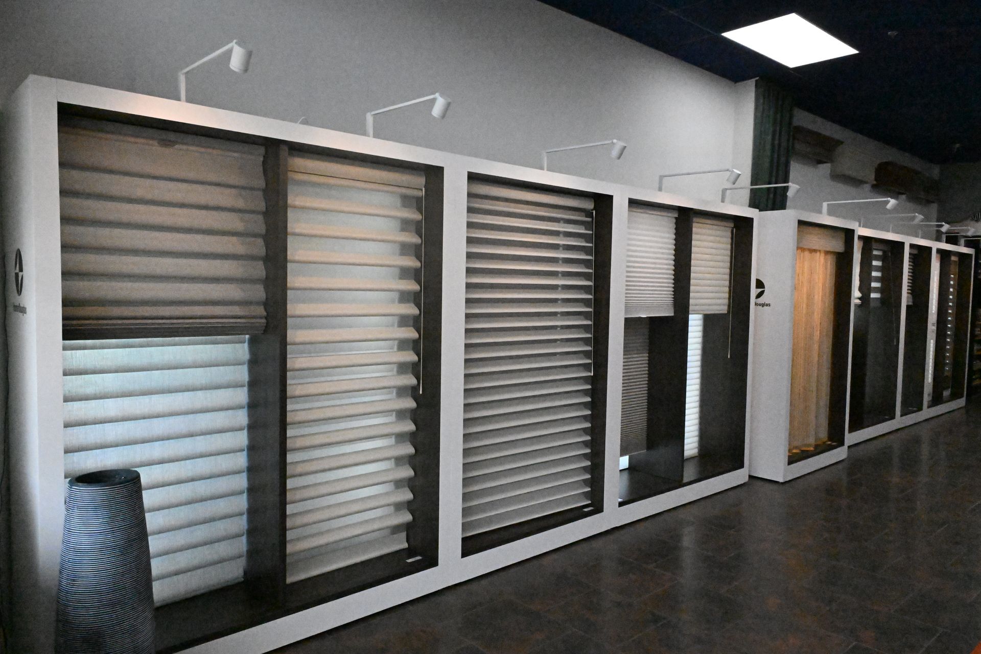 A showroom display featuring a row of various window blinds and shades in neutral tones.