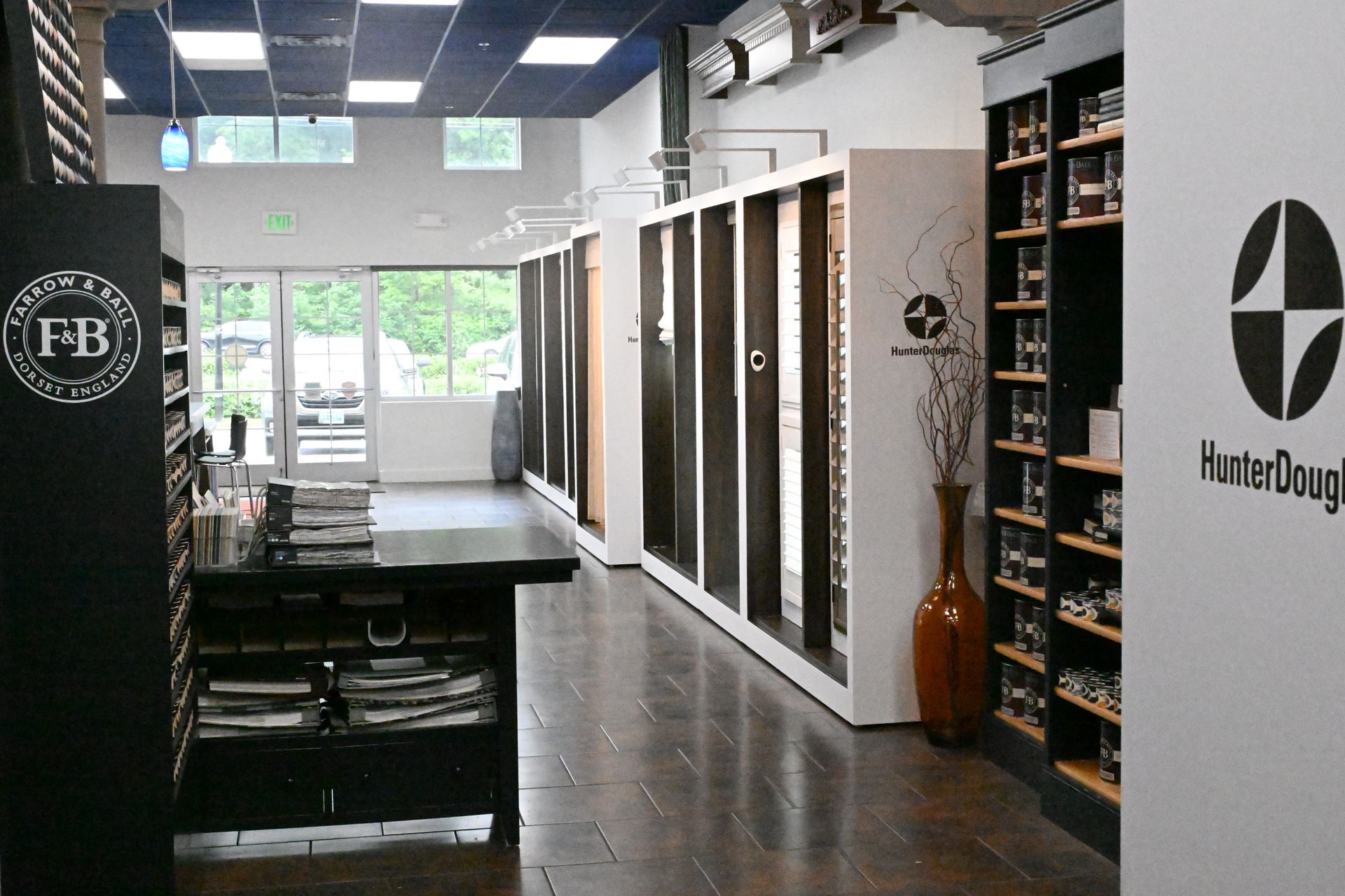 A showroom interior with Farrow & Ball paint displays, Hunter Douglas blinds, and a central counter on a wooden floor.