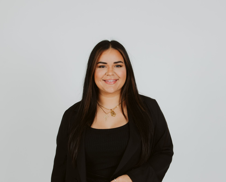 Smiling person with long dark hair in a black blazer against a light gray background