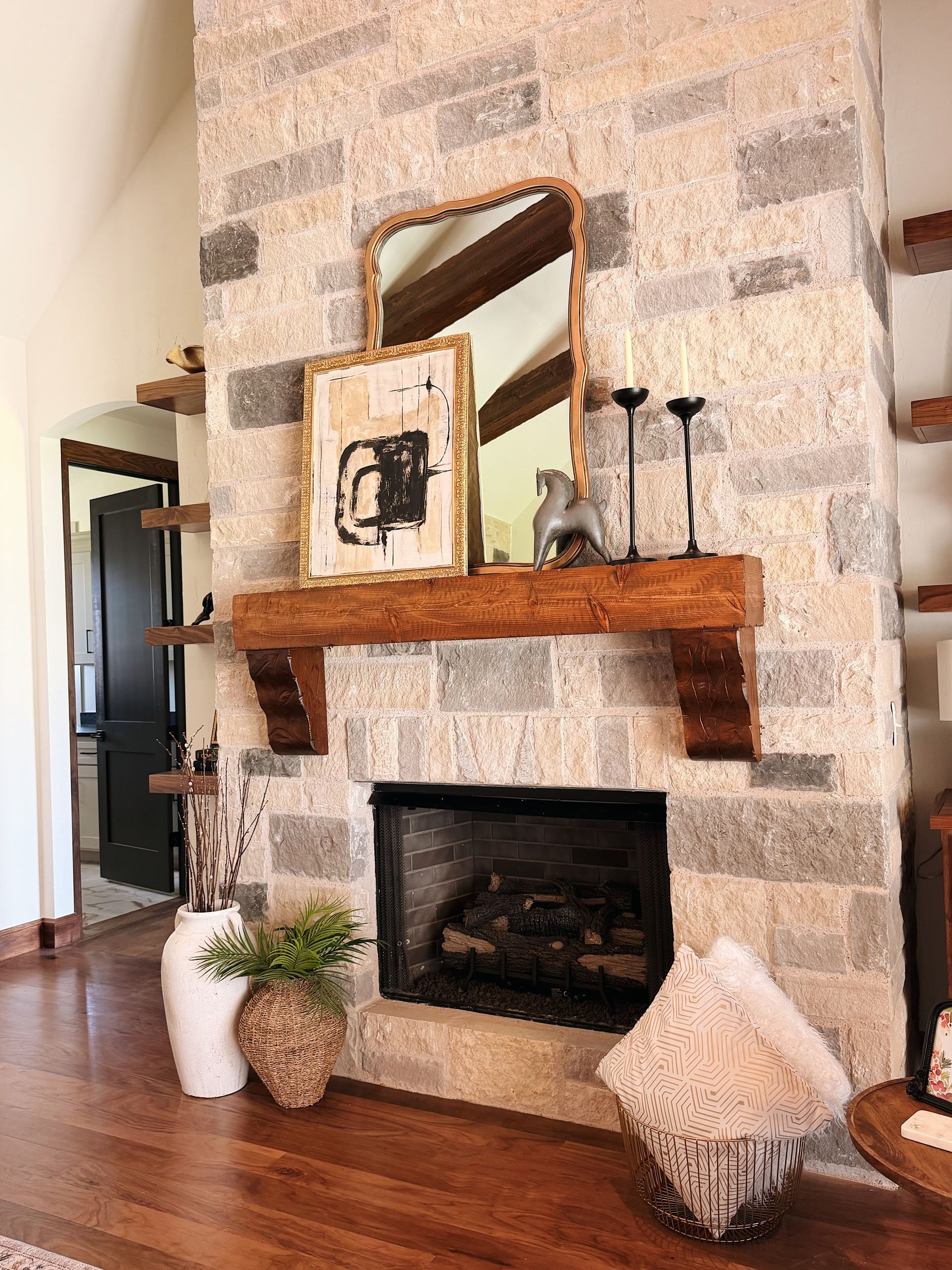 Stone fireplace with wooden mantel, mirror, and decor in a cozy living room