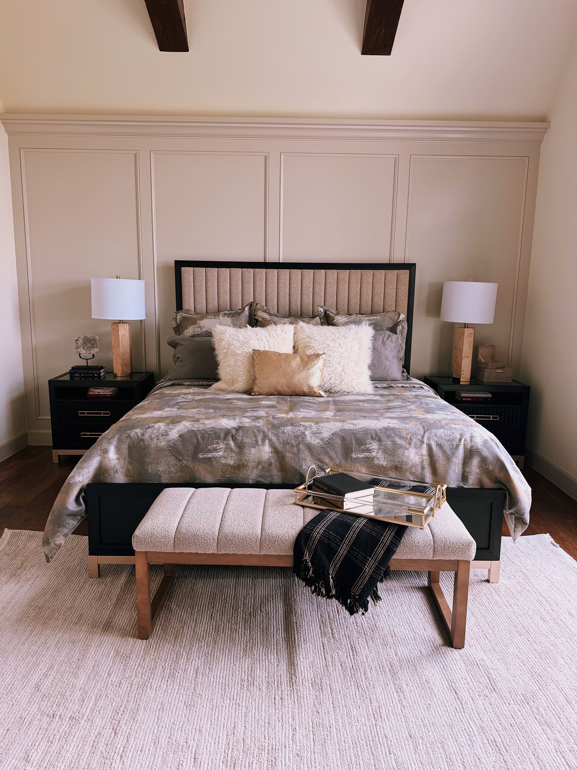 Elegant bedroom with a made bed, matching nightstands, lamps, and a patterned bench at the foot of the bed.