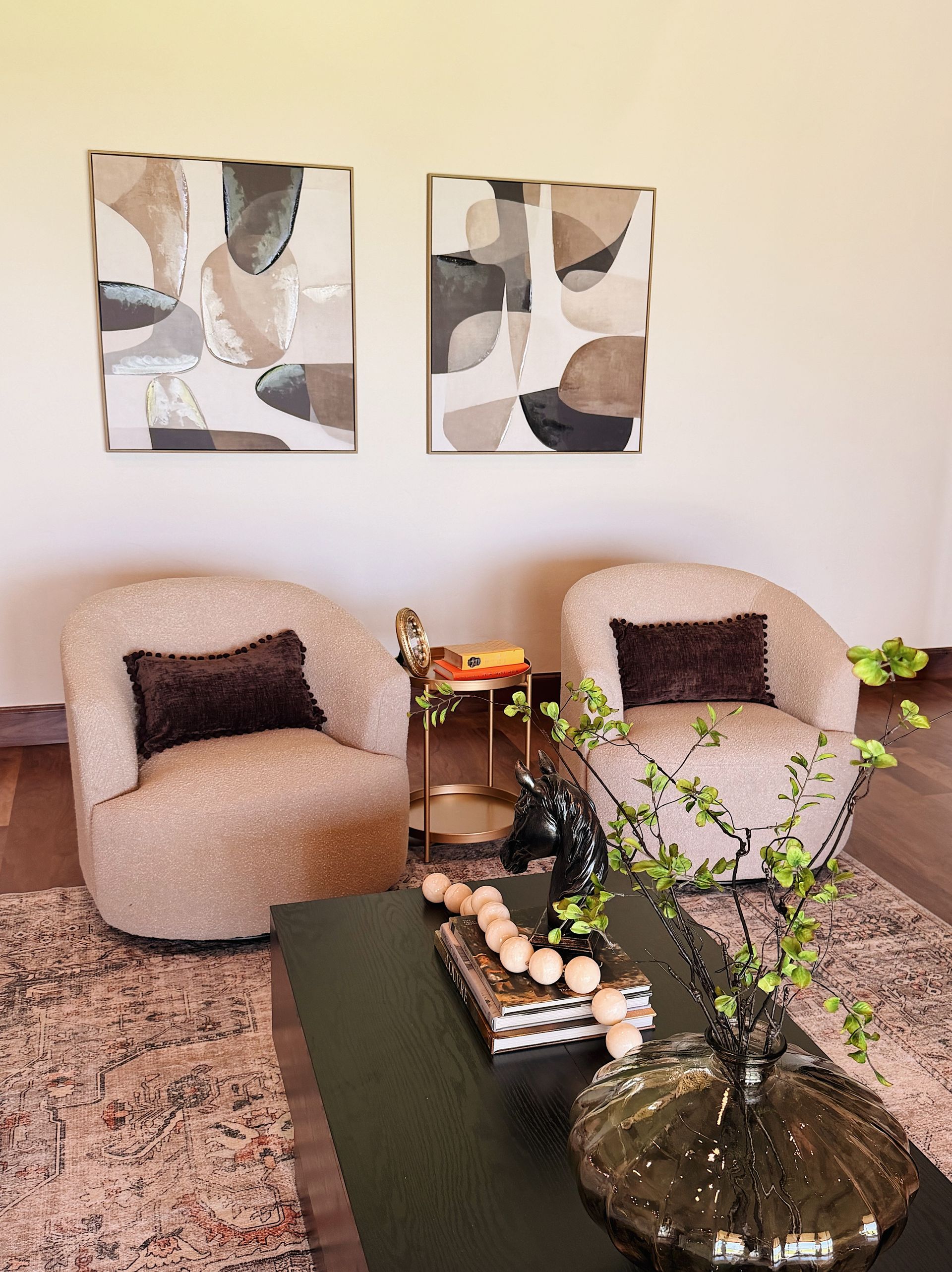 Cozy seating area with two beige chairs, abstract wall art, a coffee table, and a potted plant