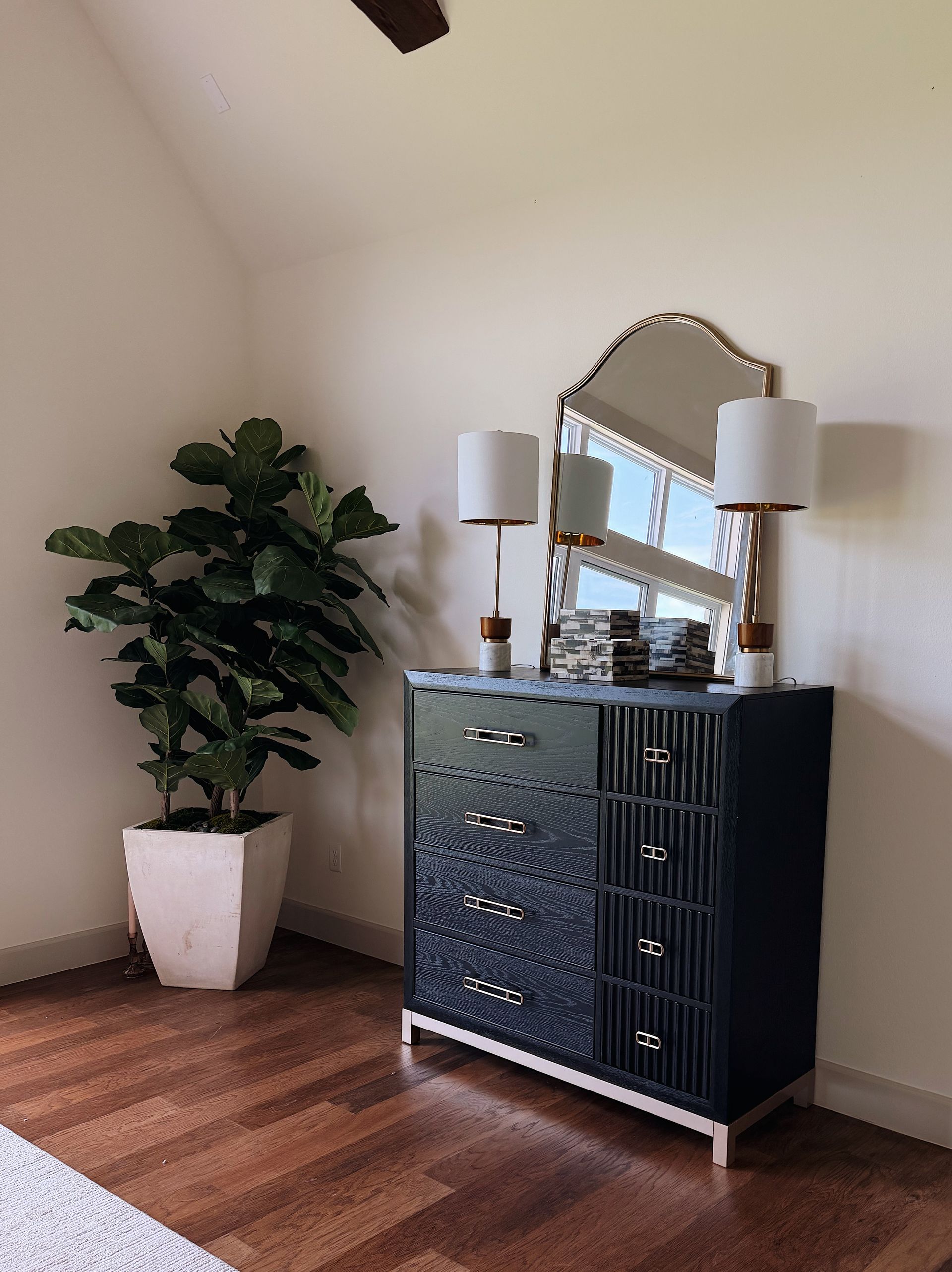 Small room with a dark dresser, mirror and lamps, a potted plant, and wood flooring.