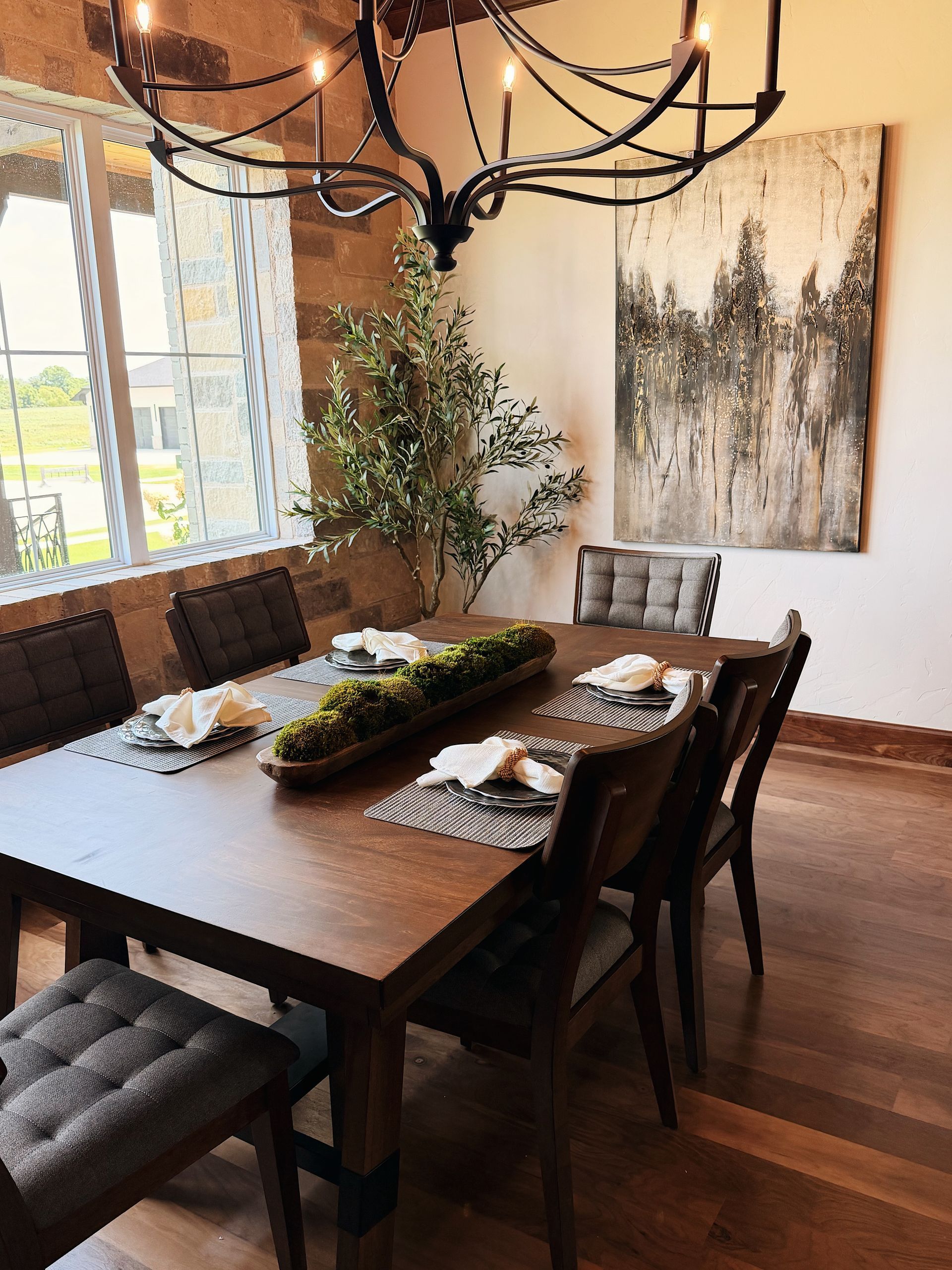Modern dining room with a wooden table, upholstered chairs, chandelier, and abstract wall art