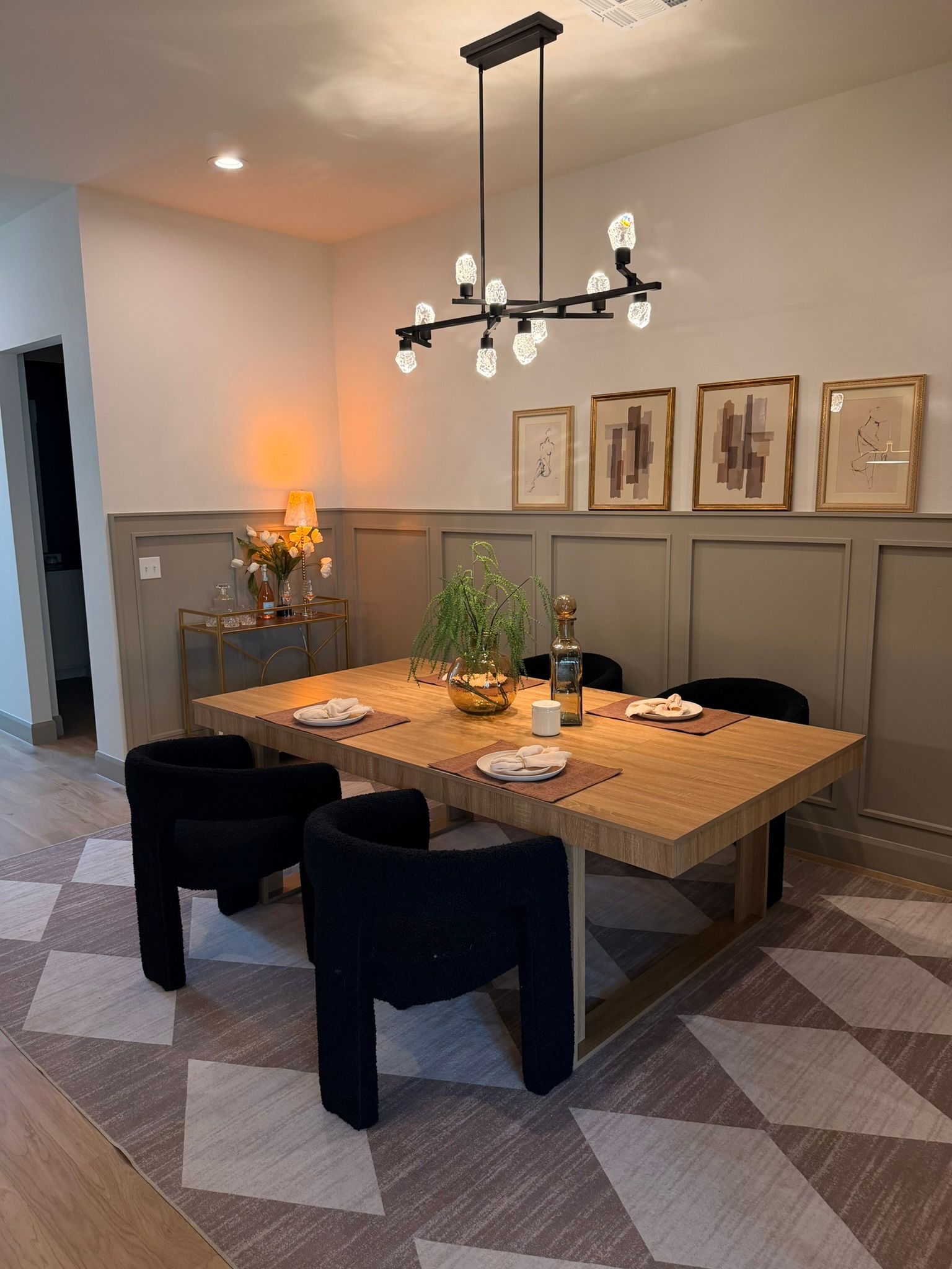 Modern dining room with a rustic table, black chairs, pendant light, and framed wall art.