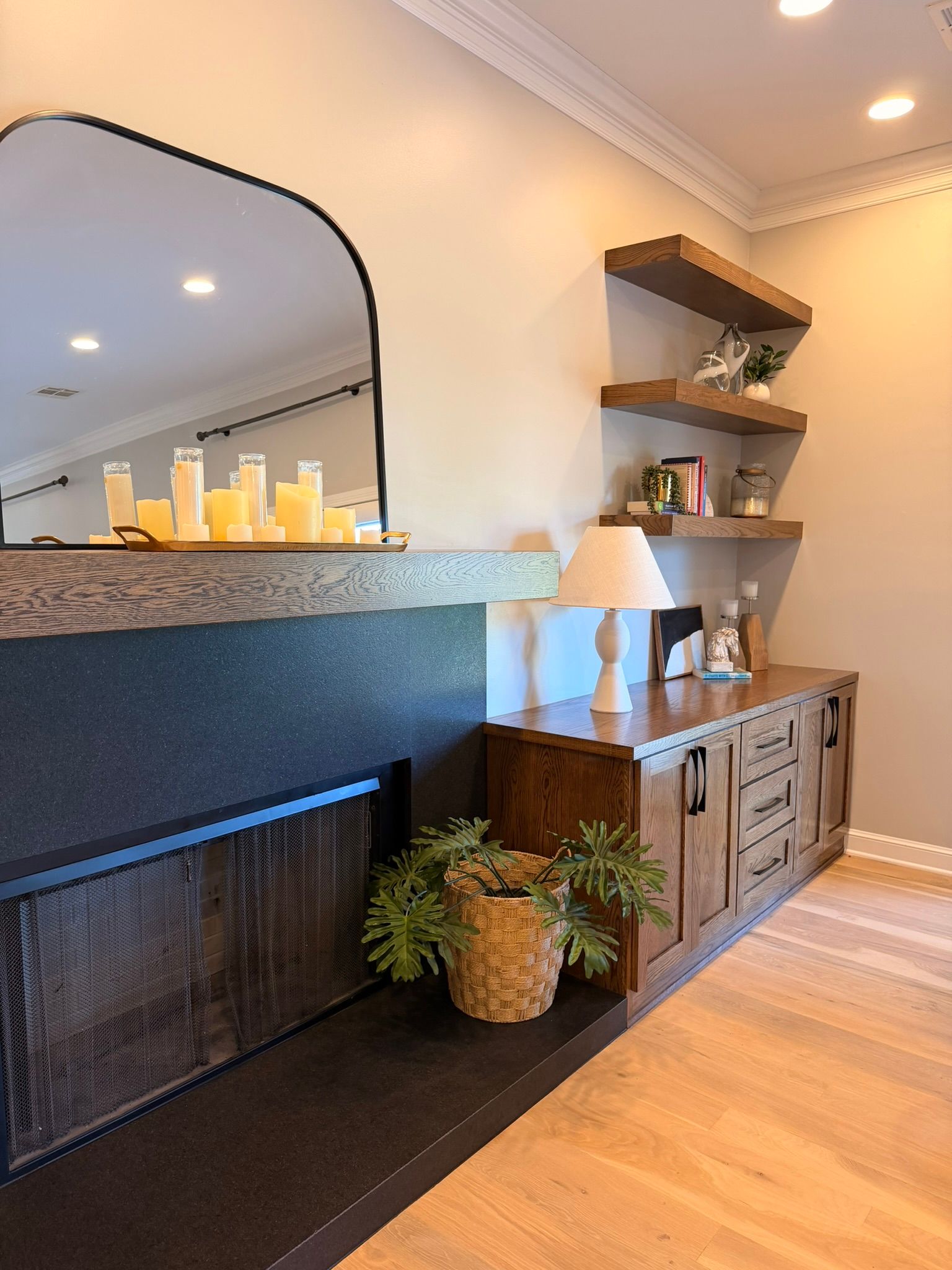 Living room mantel with mirror, candles, lamp, cabinet, and potted plants on hardwood floor