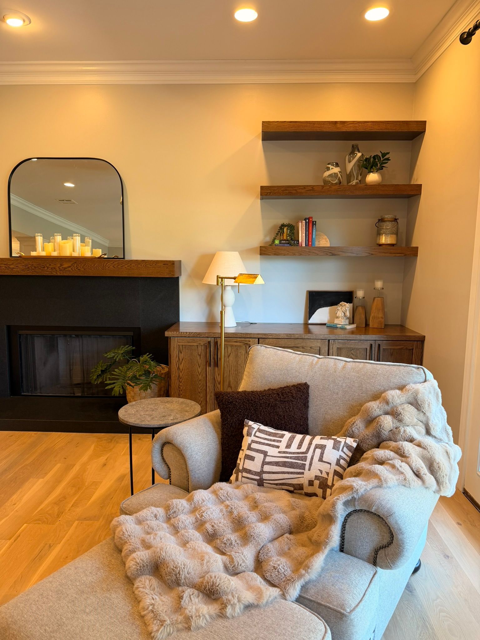 Cozy living room with armchair, fireplace, shelves, mirror, and warm lighting