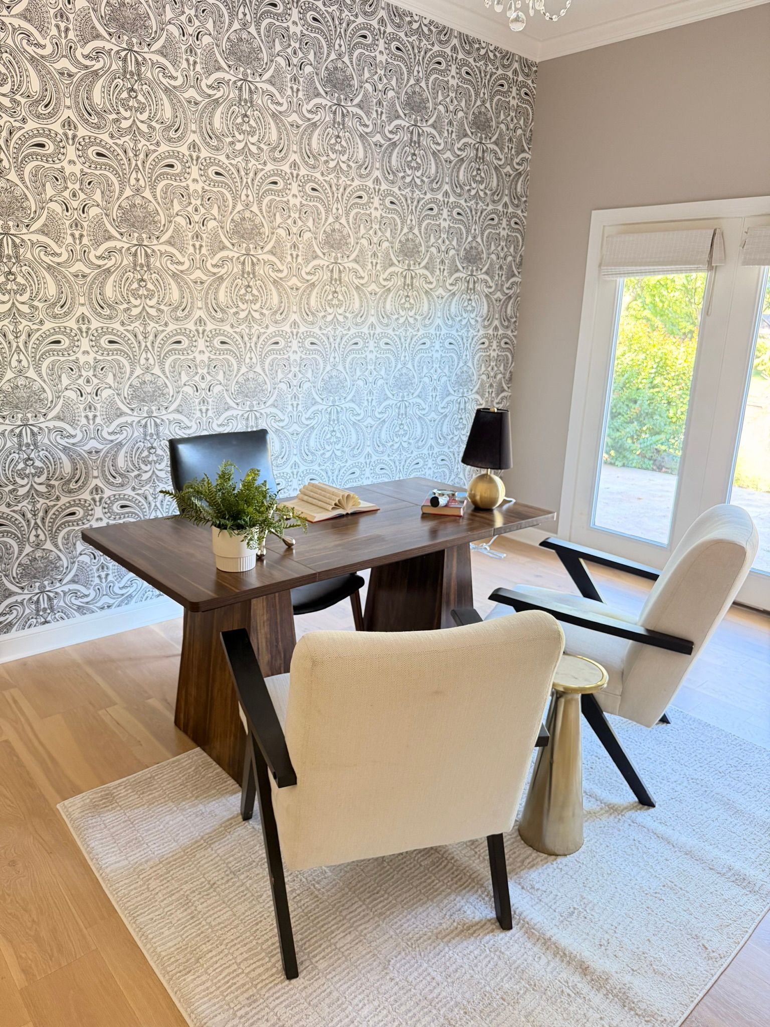 Modern dining room with a wooden table, two upholstered chairs, patterned wallpaper, and large windows.