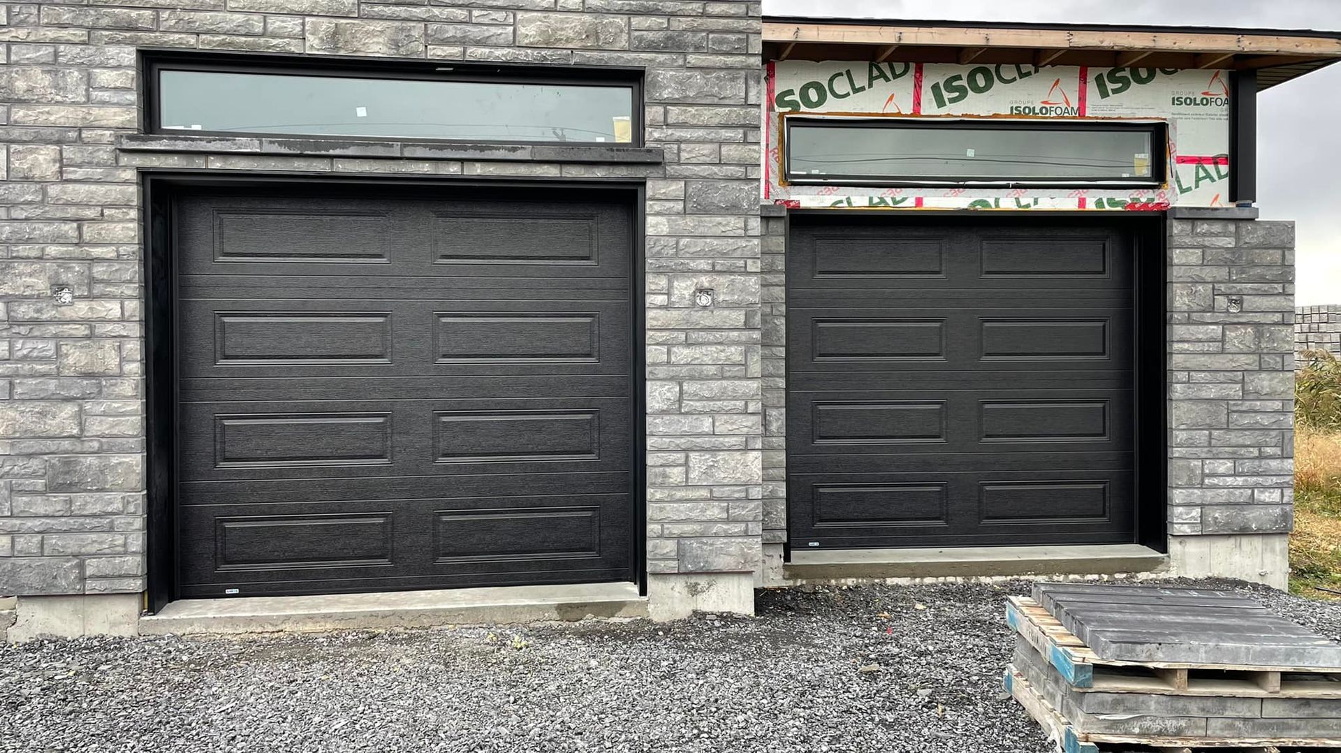 Deux portes de garage noires se trouvent devant un bâtiment en briques.
