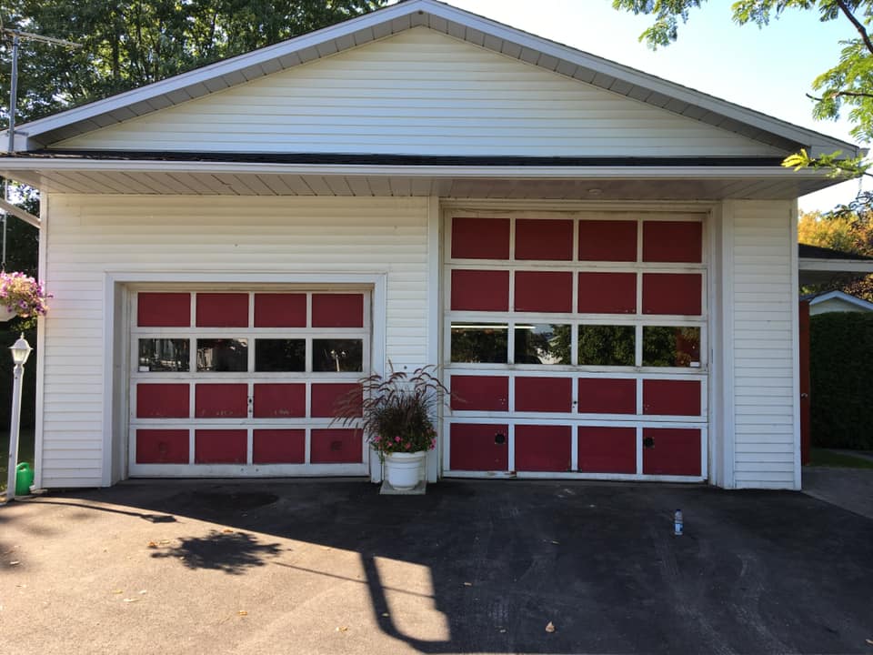 Une maison blanche avec des portes de garage rouges et une allée
