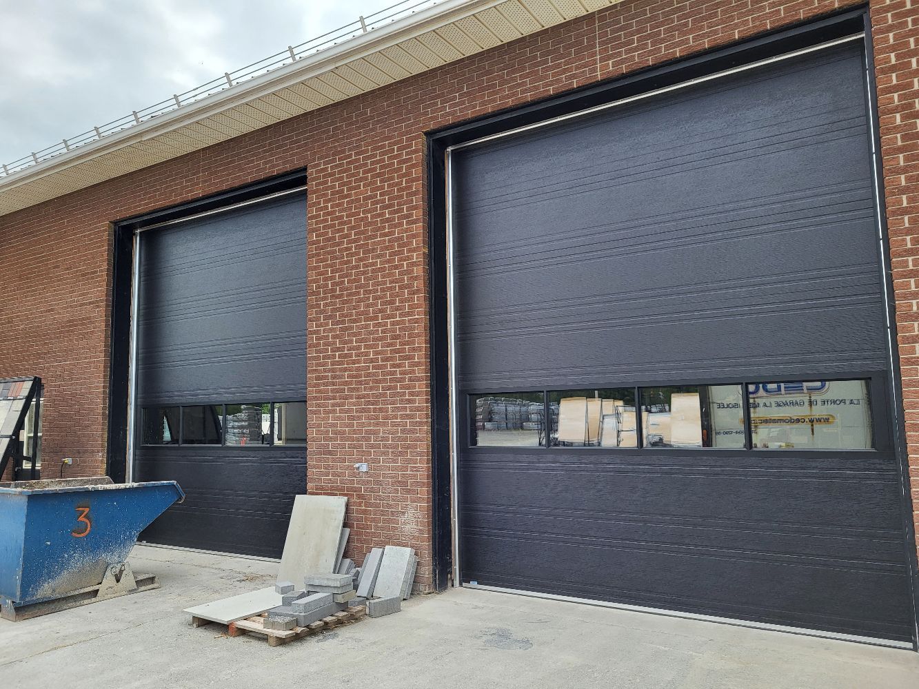 Deux portes de garage noires sont placées sur le côté d'un bâtiment en briques.
