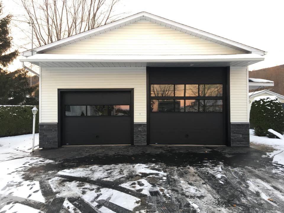 Un garage avec une porte noire et un revêtement blanc est dans la neige.