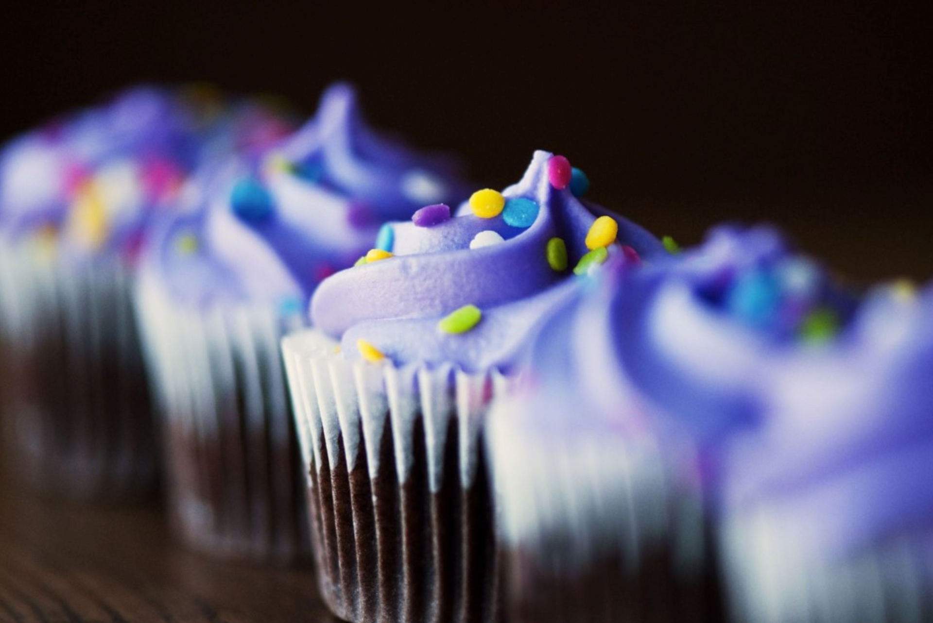 A row of cupcakes with purple frosting and sprinkles on a table.