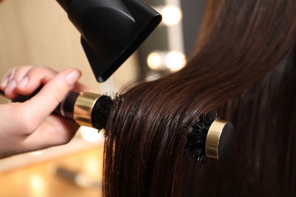 Hair being styled with a round brush and hairdryer; dark brown hair.
