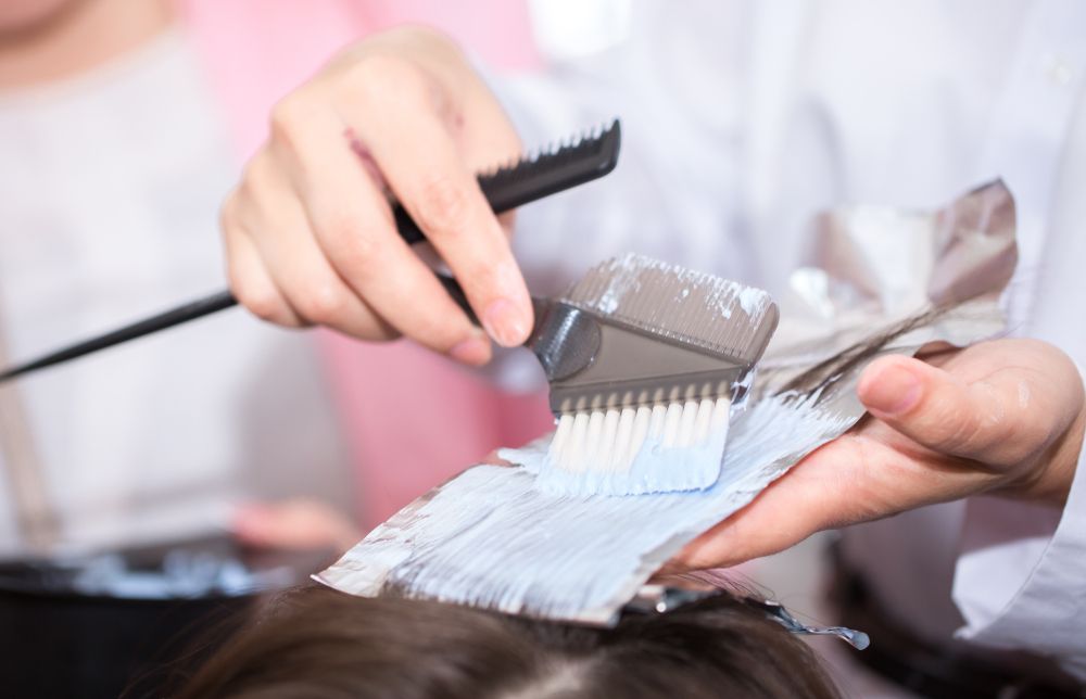 Hairdresser applying hair dye with brush onto foil-wrapped hair strands.