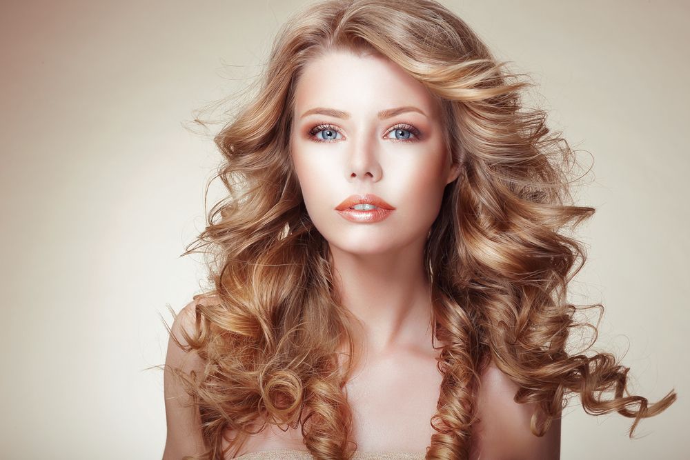 Woman with blonde, curly hair, blue eyes, and light skin, looking toward the camera.