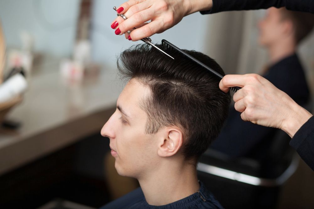 A person getting a haircut, stylist using scissors and comb. Indoors, neutral colors.