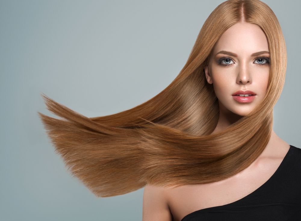 Woman with smooth, flowing, auburn hair, wearing a black top, with a neutral background.