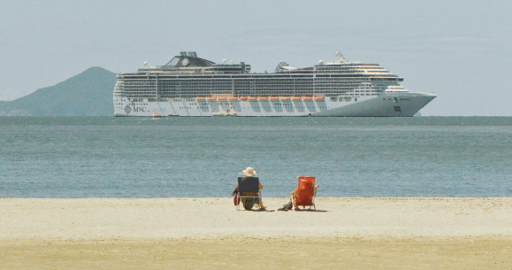 Casal sentado em cadeiras de praia vendo um navio de cruzeiro em Balneário Camboriú