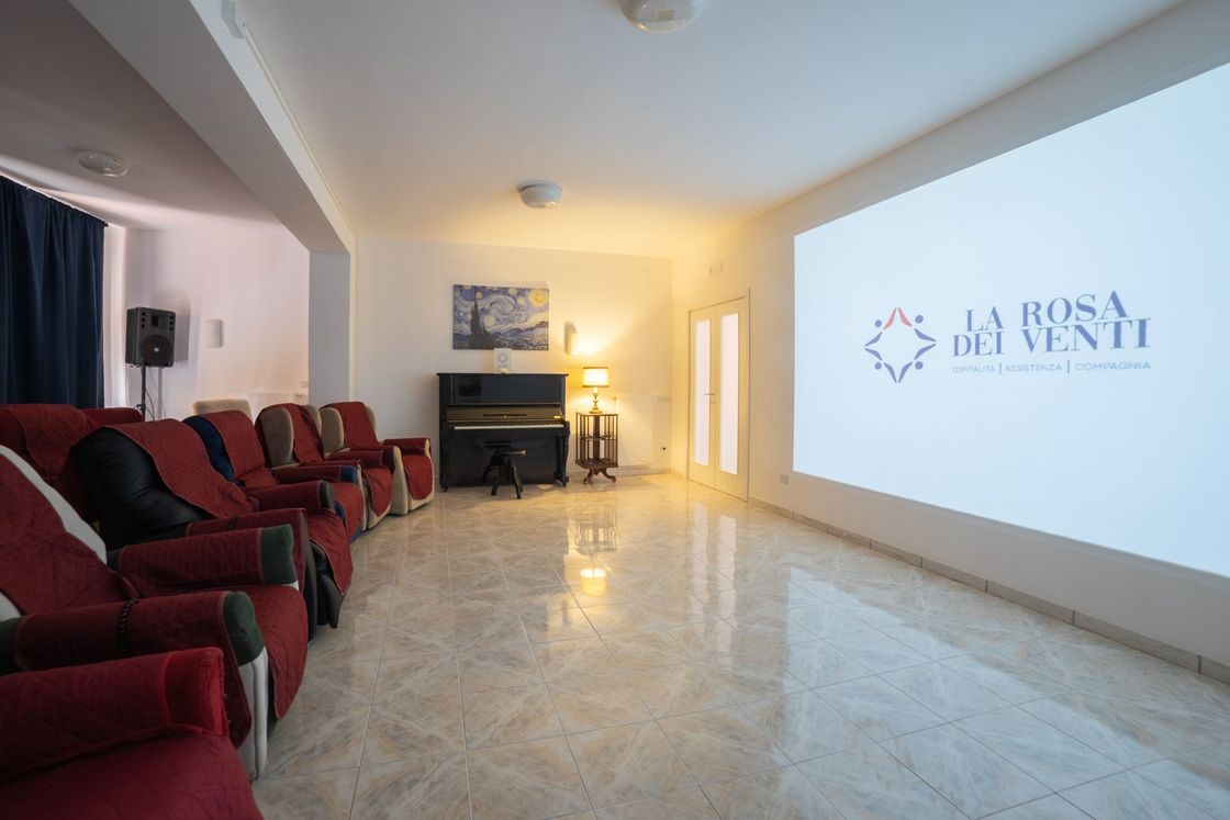 Una sala cinematografica accogliente con file di poltrone rosse, un pianoforte in un angolo e un grande schermo che mostra il logo dell'azienda.
