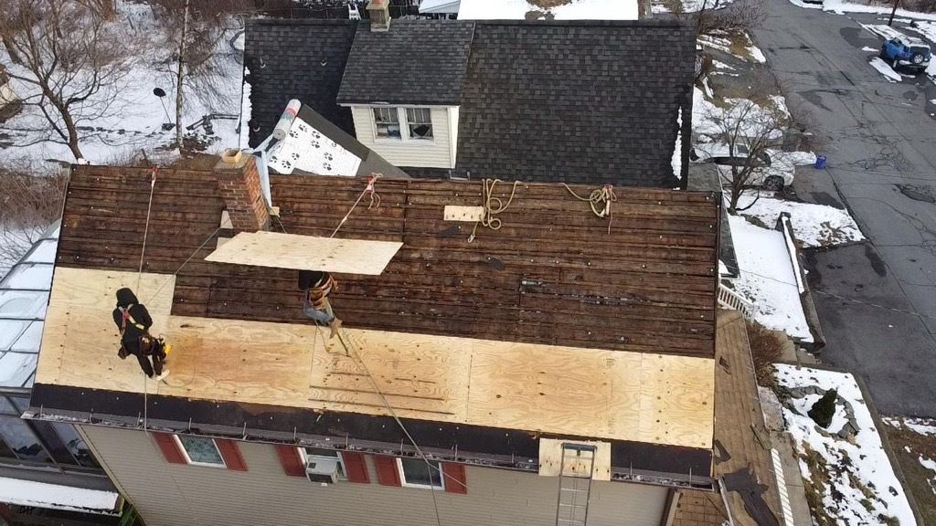 Damaged house roof with missing shingles in snowy residential area.