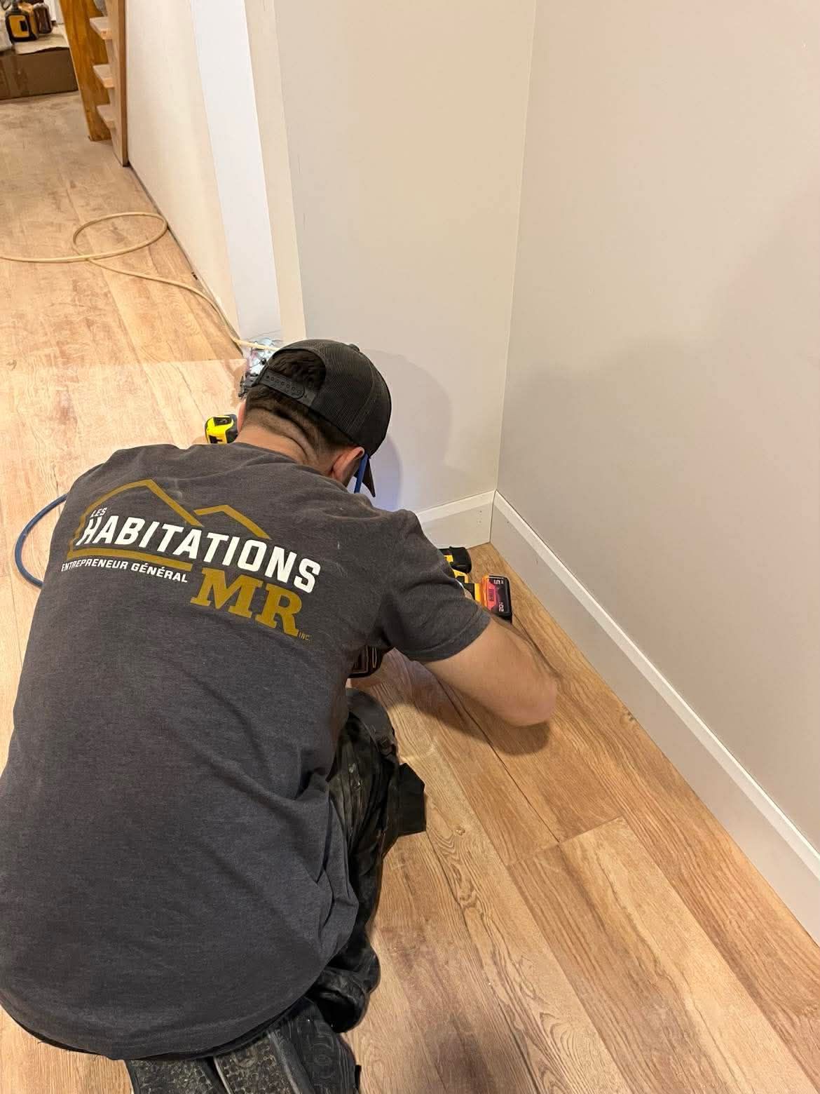 Une personne installe des lames de parquet, portant des gants, dans une pièce avec un mur en béton et des outils de mesure.