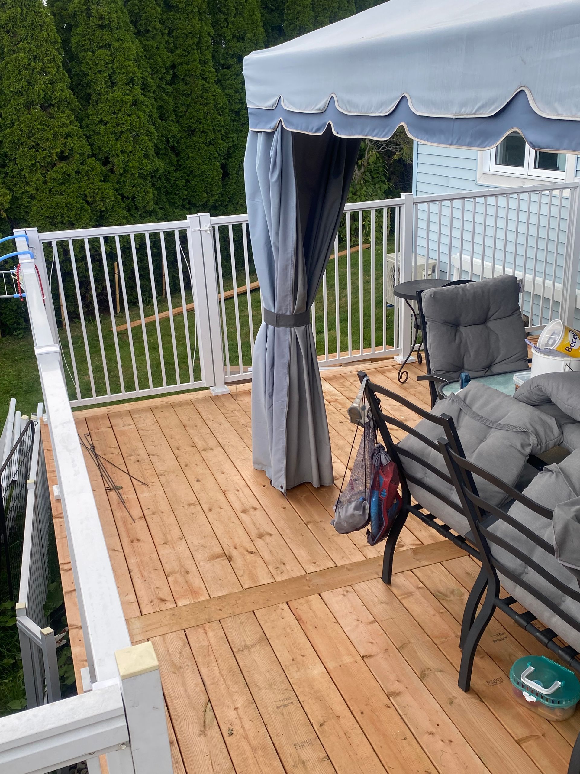 Terrasse en bois avec rambarde blanche, auvent bleu et mobilier de jardin.