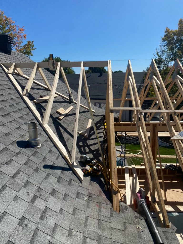 Construction du toit en cours, avec charpente et fermes en bois, sur fond de ciel bleu dégagé.