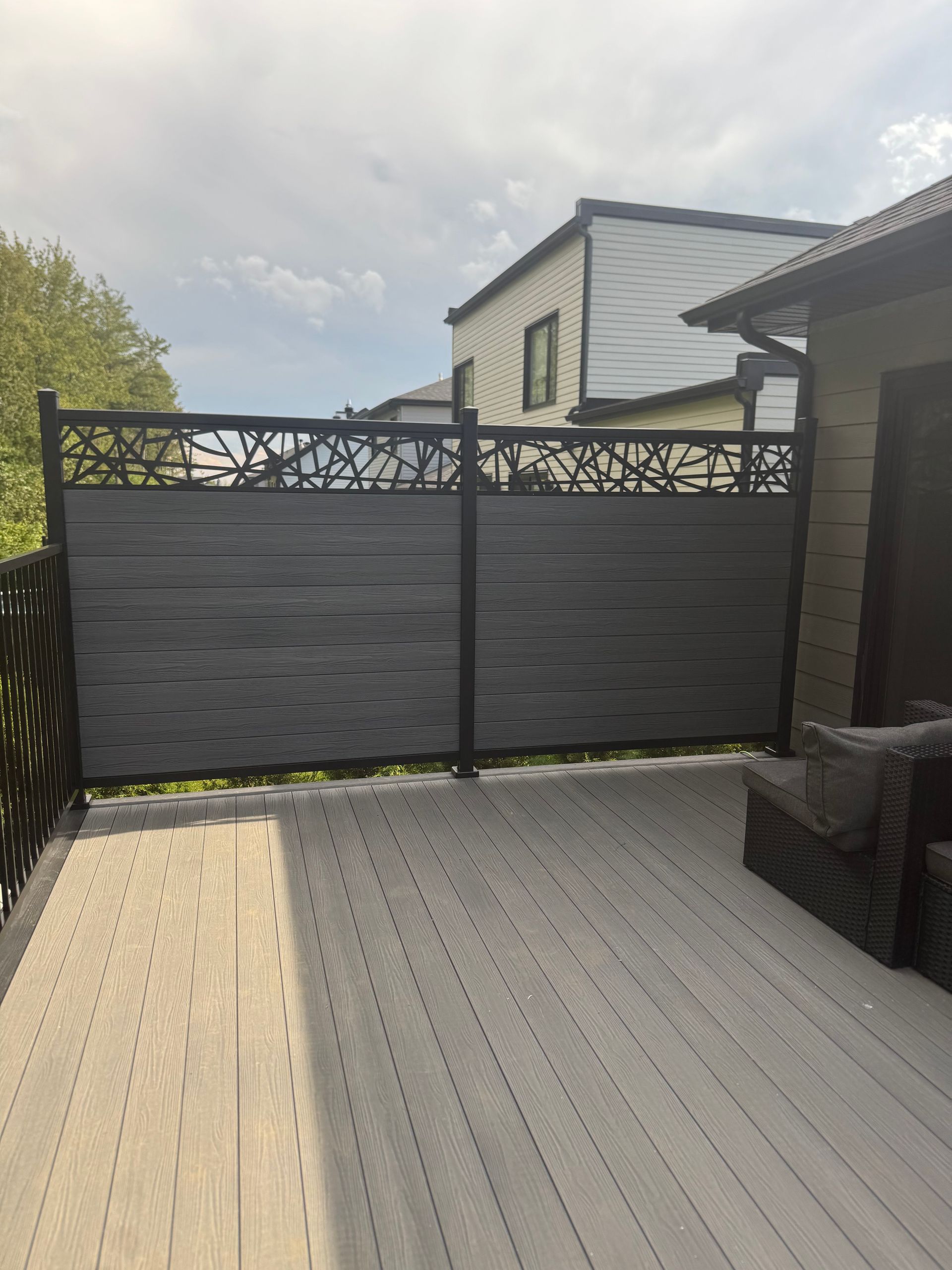 Terrasse en composite gris avec une clôture d'intimité gris foncé et une partie supérieure décorative.