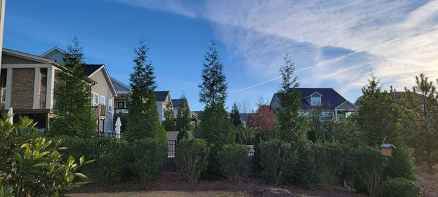 Houses with blue sky and some clouds, trees and bushes in front of the houses.