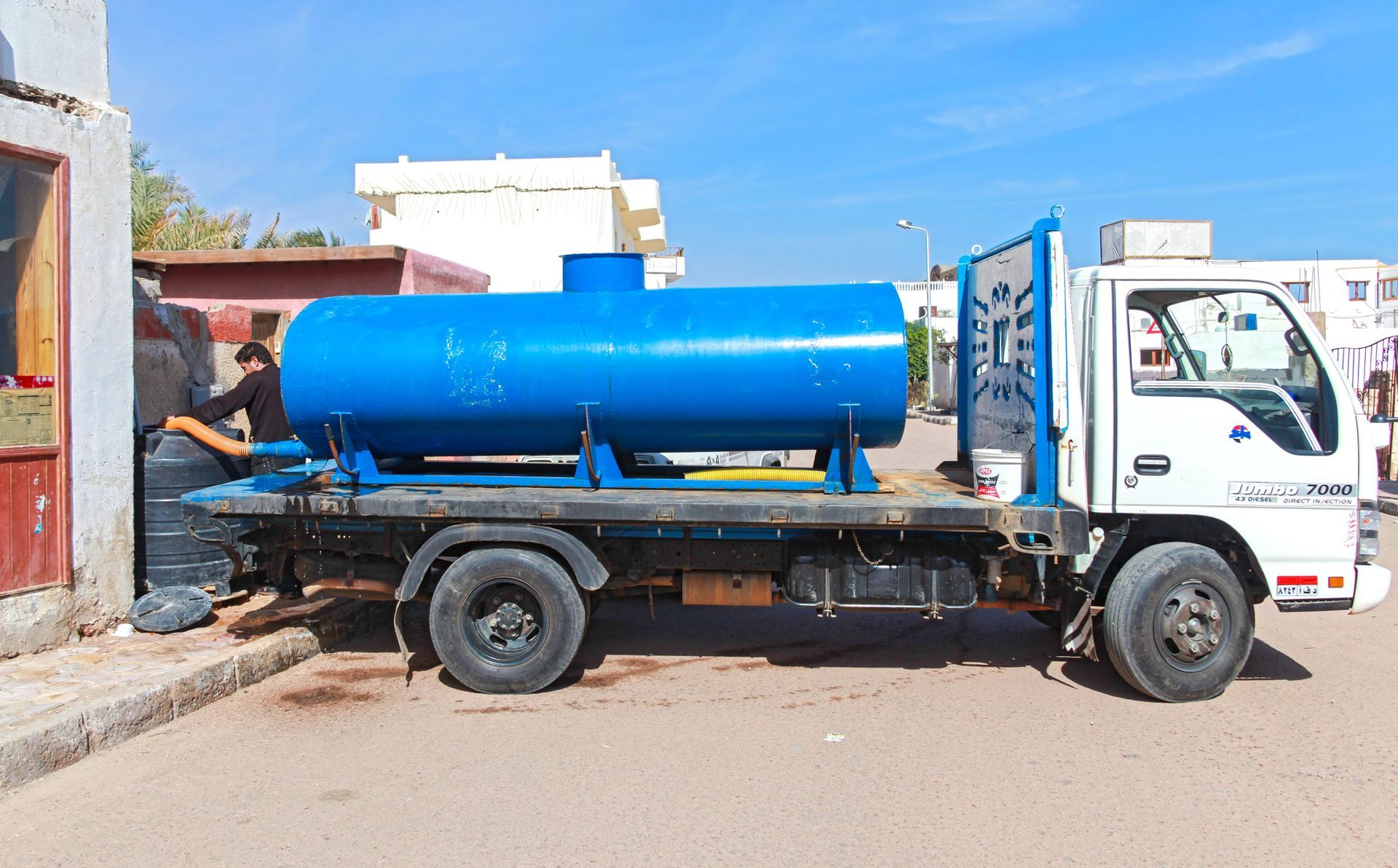 Camión cisterna azul con el rótulo «Agua Potable para la Comunidad» estacionado mientras la gente