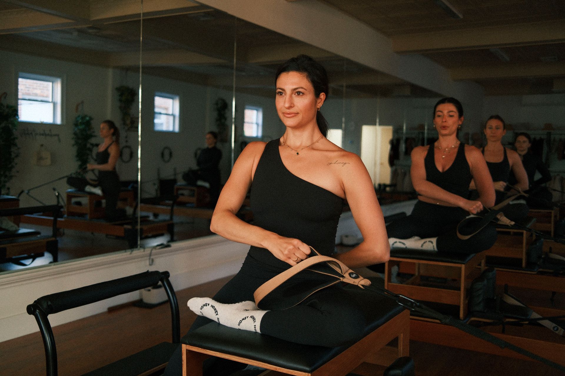 Three girls sitting on a reformer with one hand holding a strap