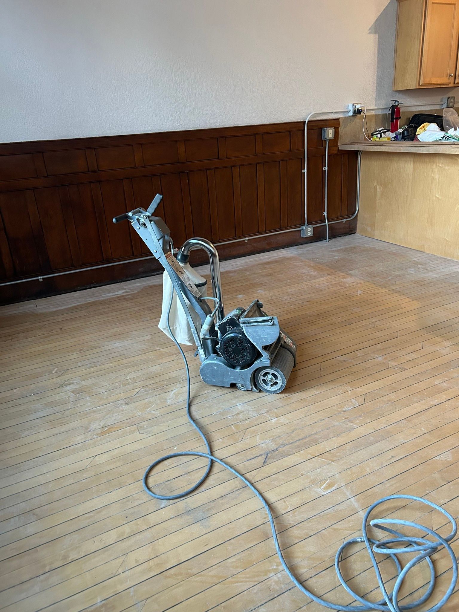 Floor grinding machine with cord in a room with wood paneling and light wood floor