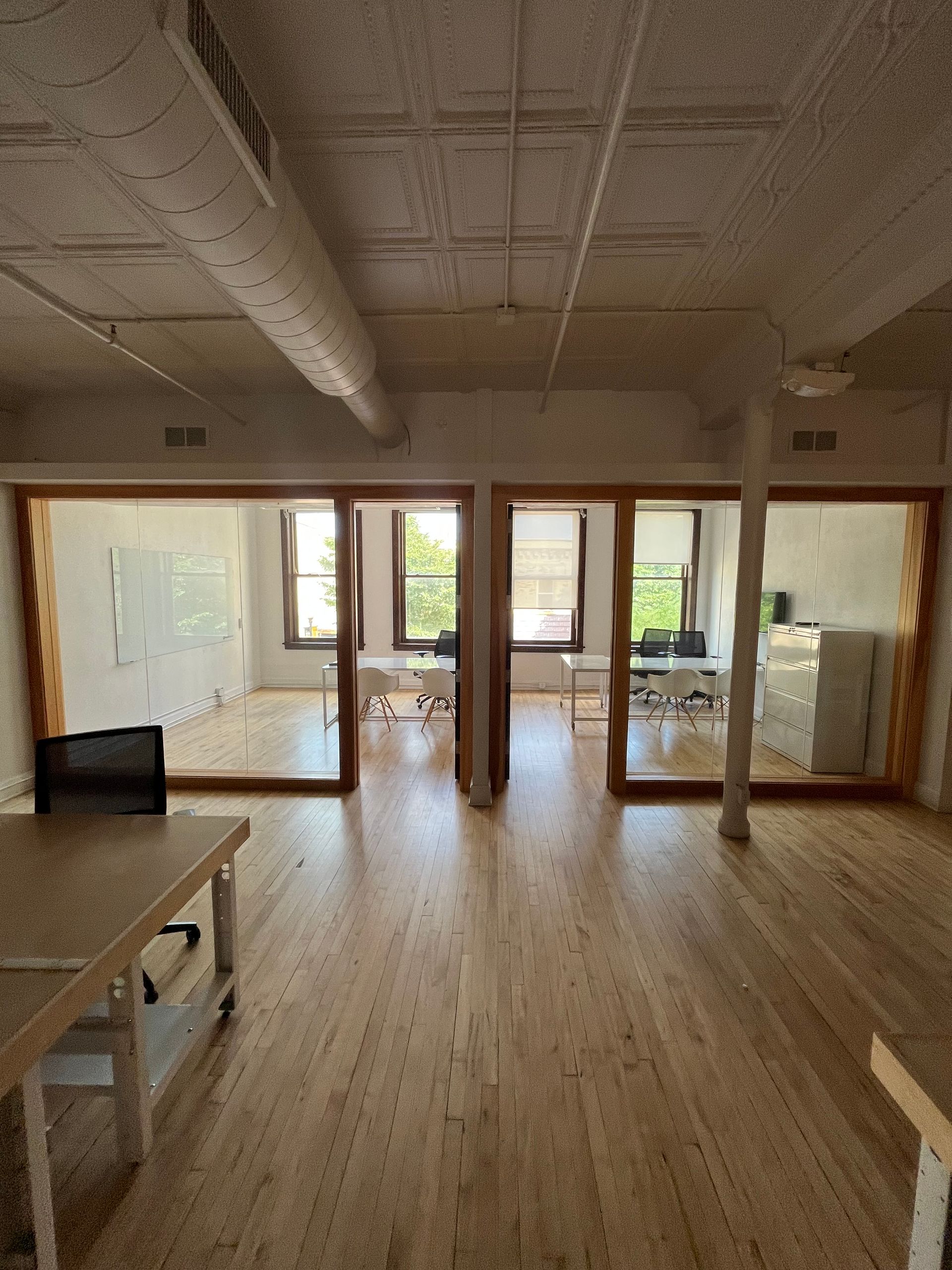 Empty office with wood floors, exposed ductwork, and glass-walled rooms.
