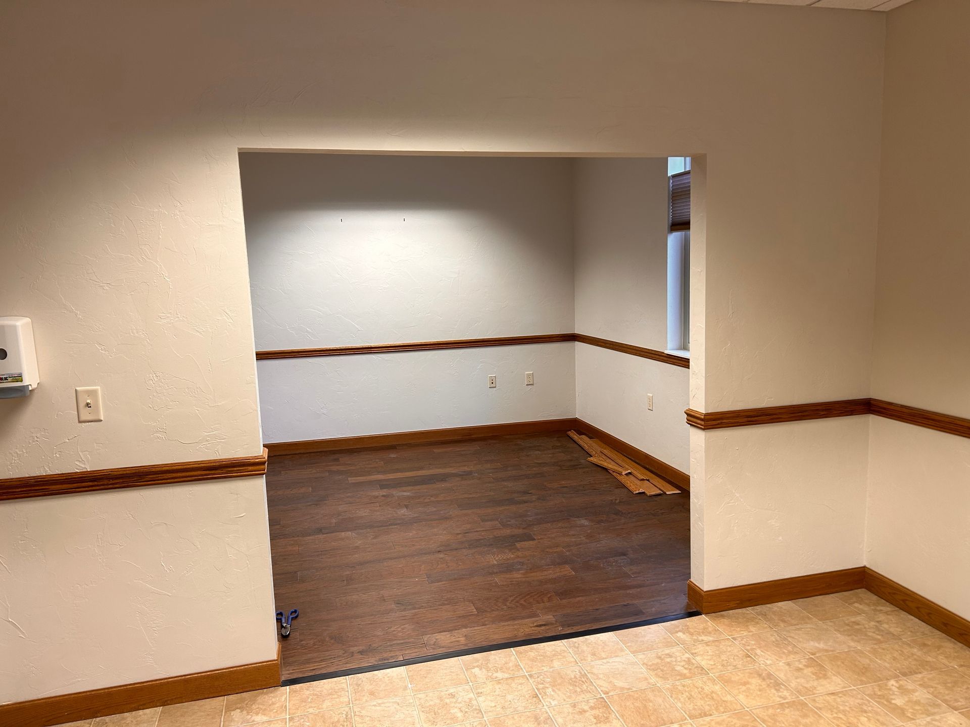 Empty beige room with brown trim and a recessed opening to a darker wood-floored space