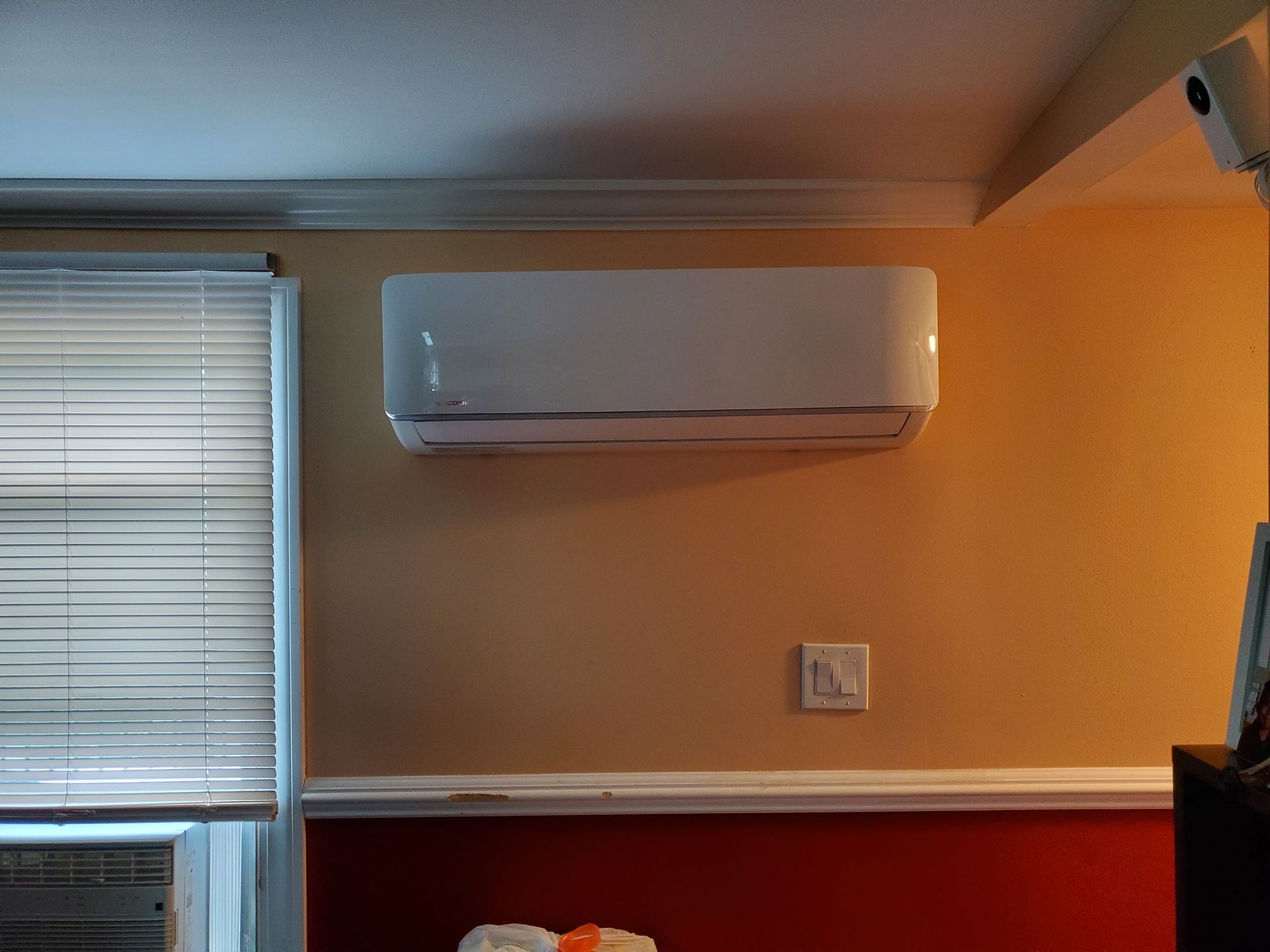A white air conditioner is mounted on a wall next to a window.