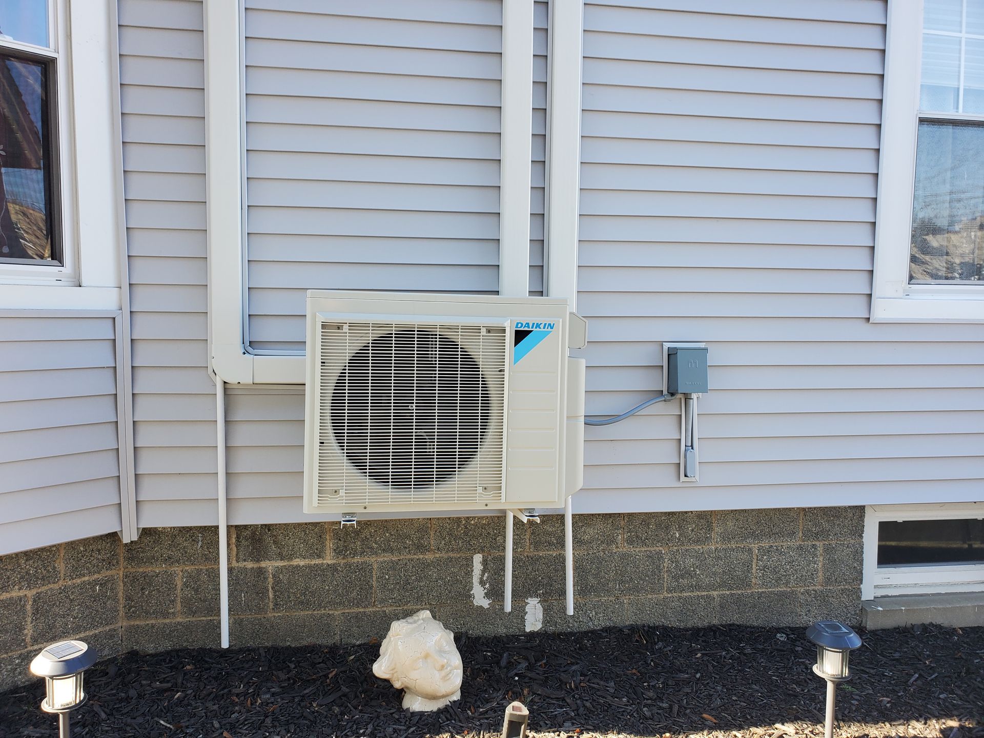 A white air conditioner is mounted on the side of a house.