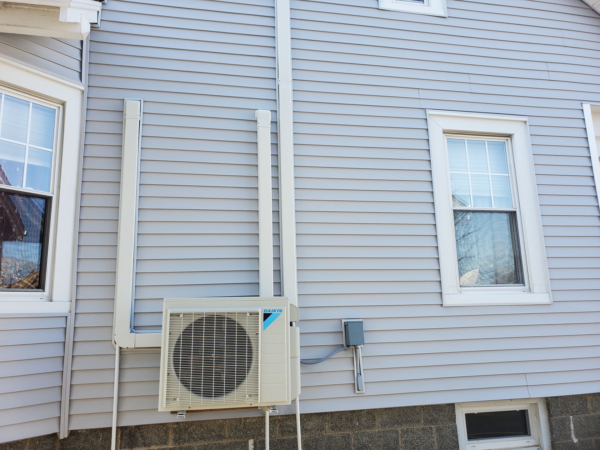 A white air conditioner is mounted on the side of a house