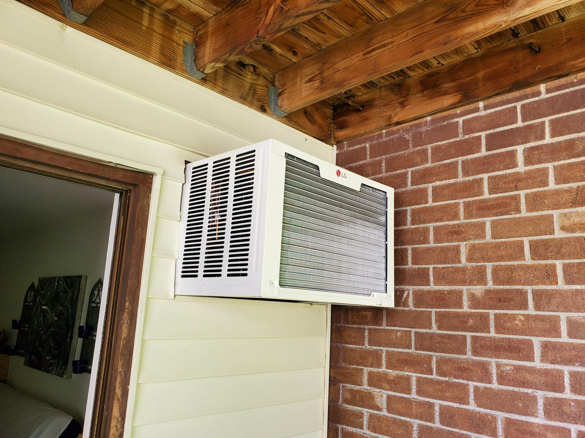 A white air conditioner is mounted on the side of a brick building.