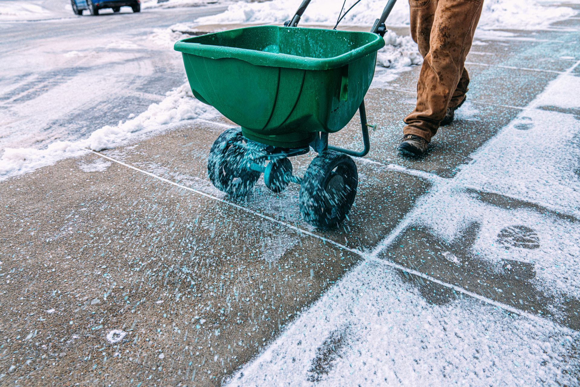 A man is spreading salt on a sidewalk with a wheelbarrow.