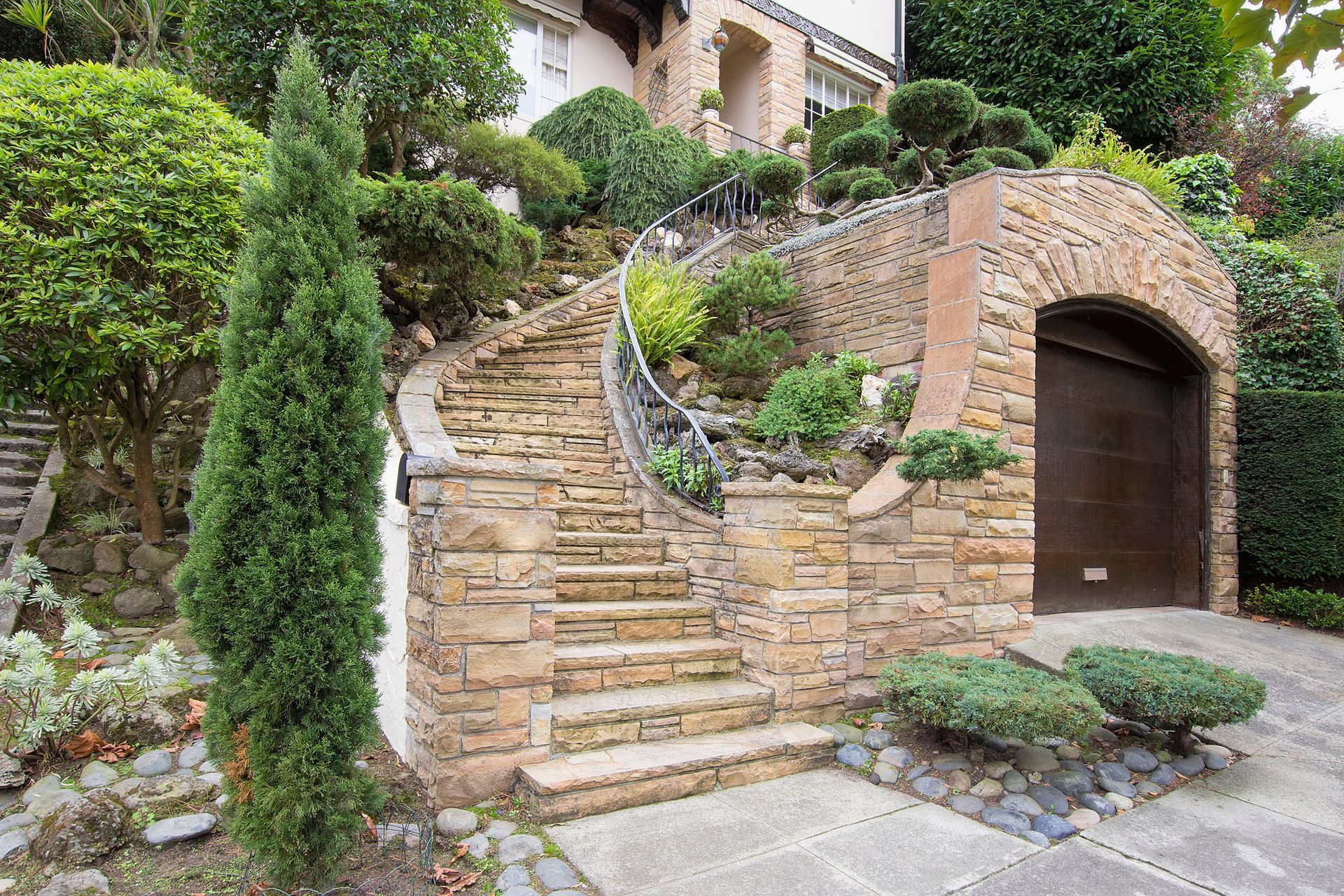 A stone wall with stairs leading up to a garage in front of a house.