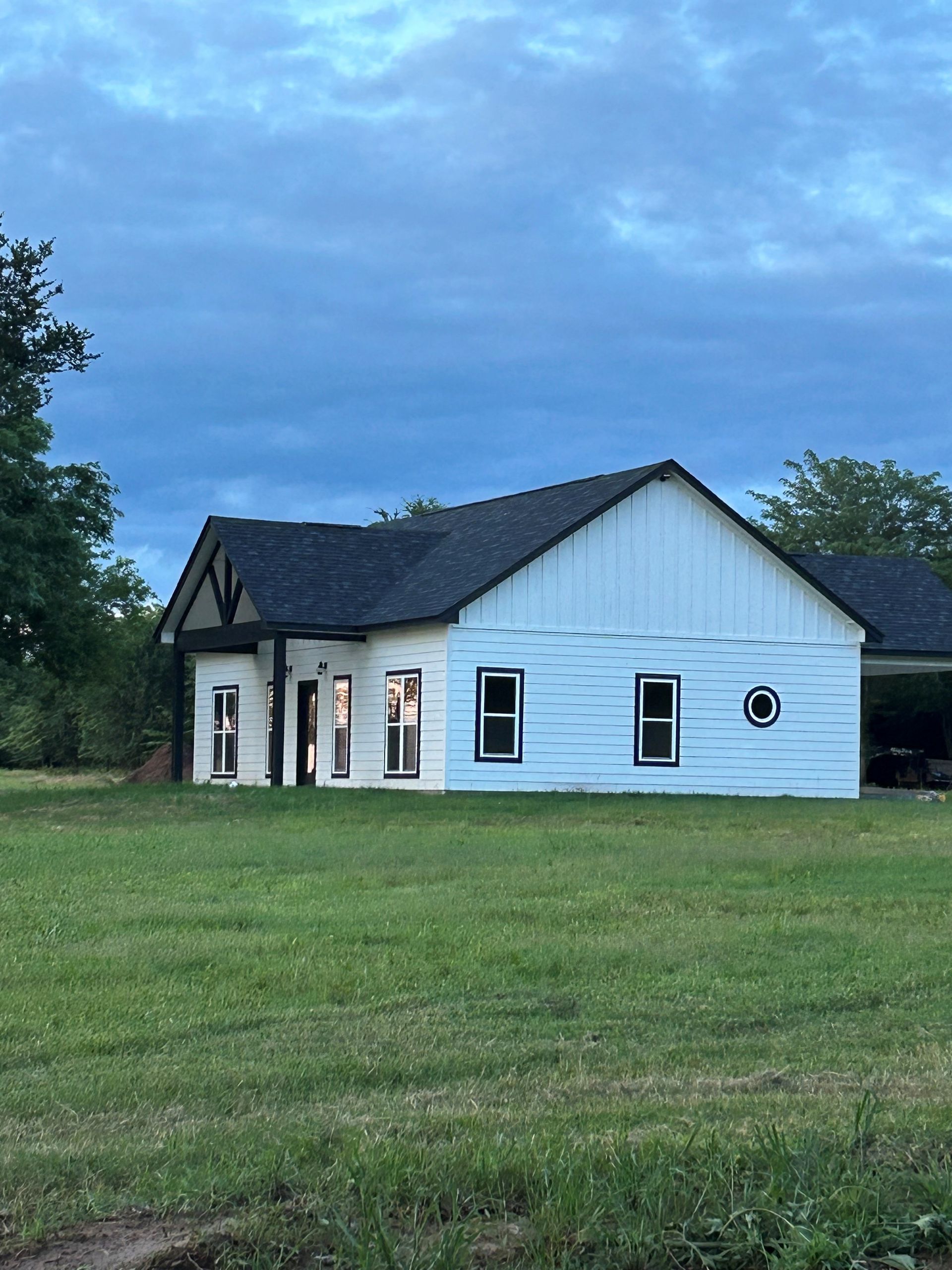 White house with dark roof in a grassy field at dusk under a blue cloudy sky