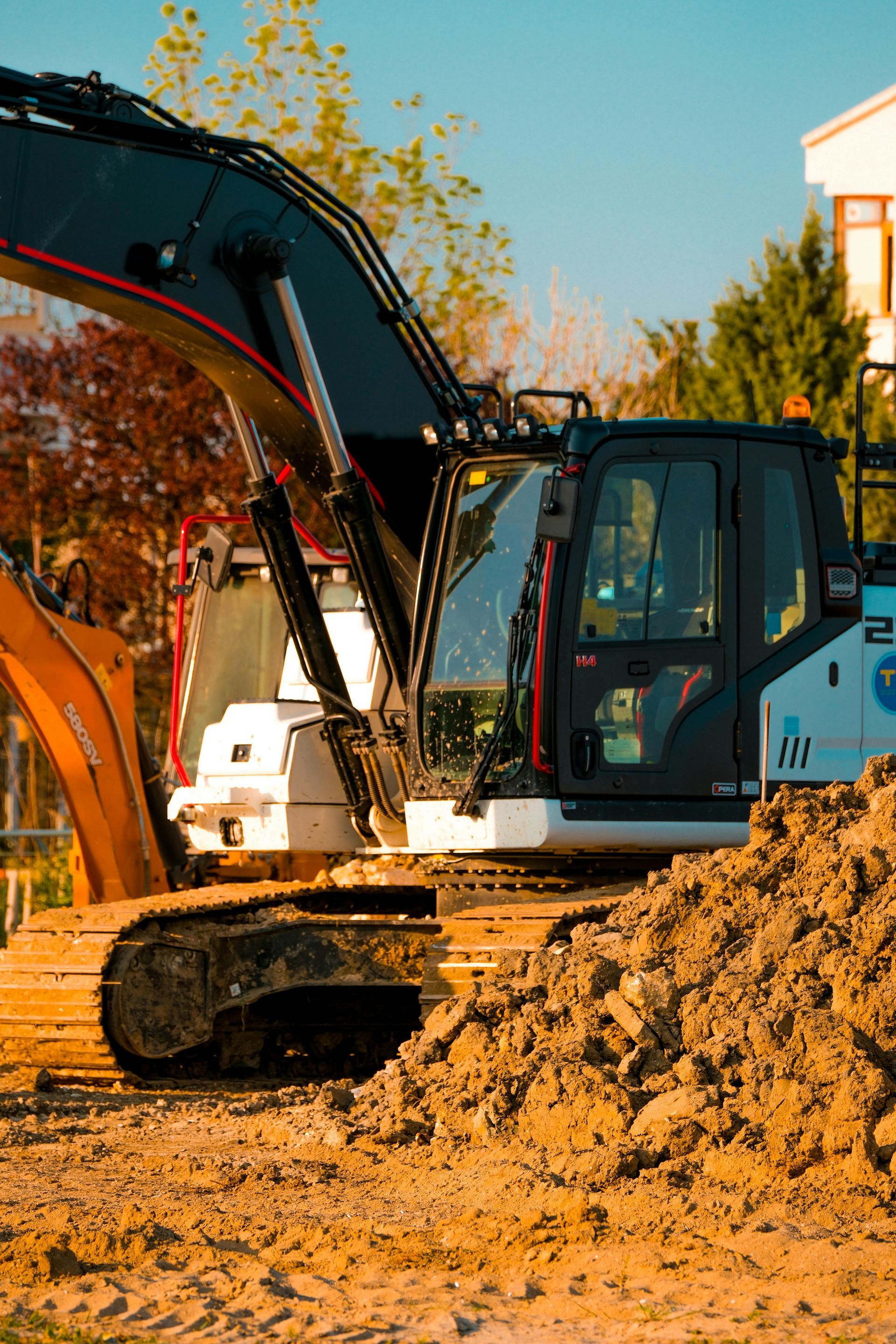 Excavator working in a muddy construction site beside a building under blue sky