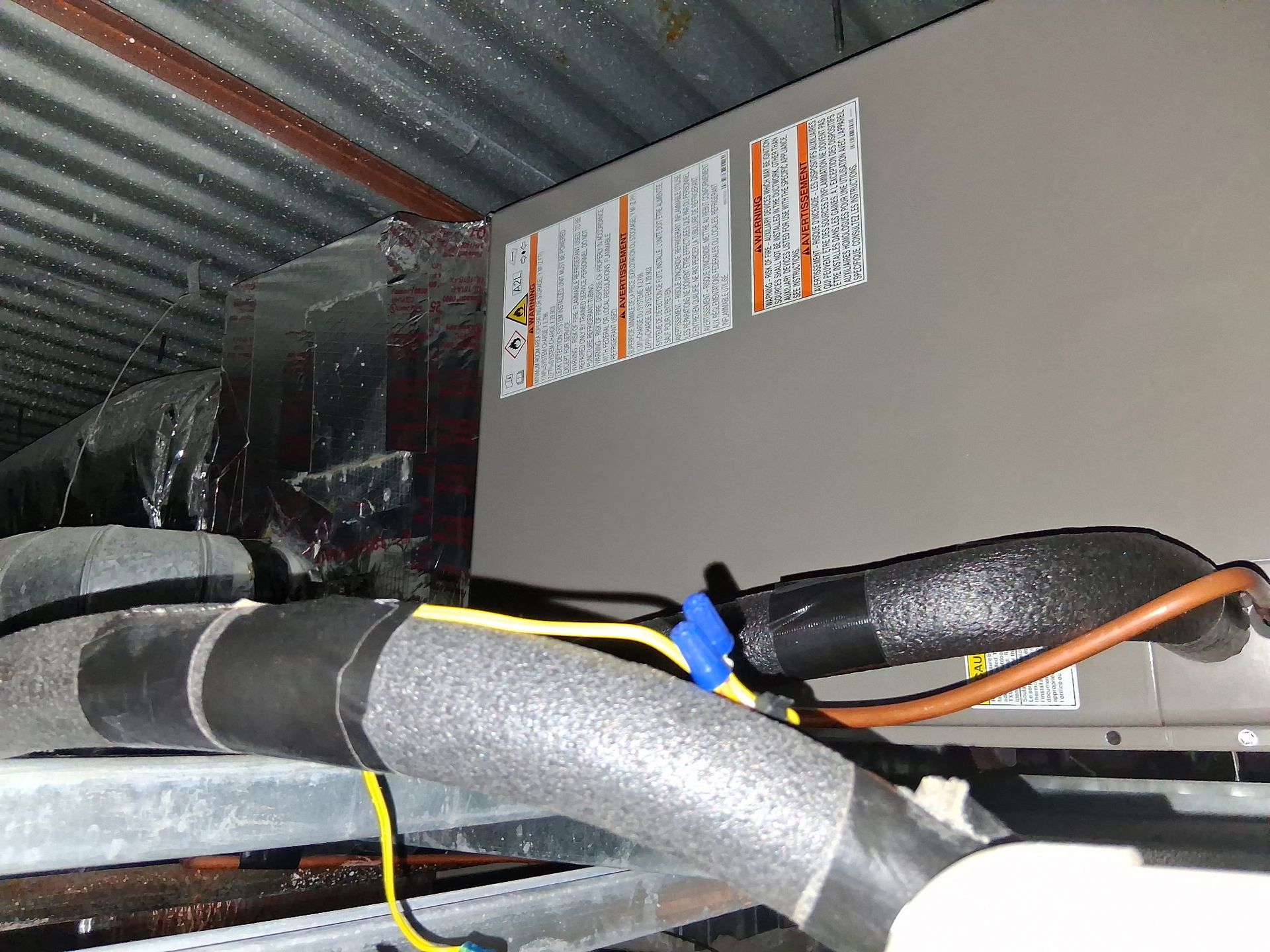 HVAC unit with insulated pipes and wiring inside a metal attic space