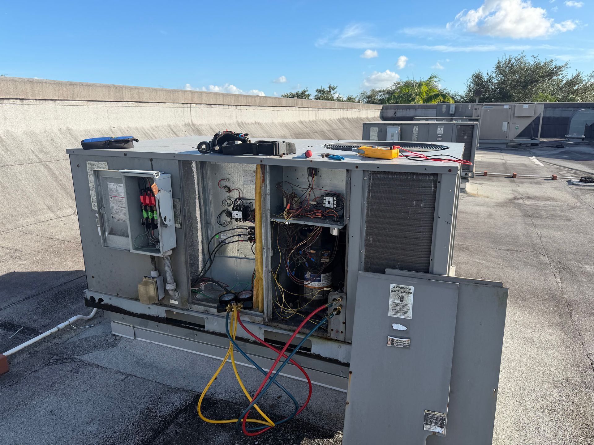 Open HVAC unit with exposed wiring and open panel on a rooftop under a blue sky
