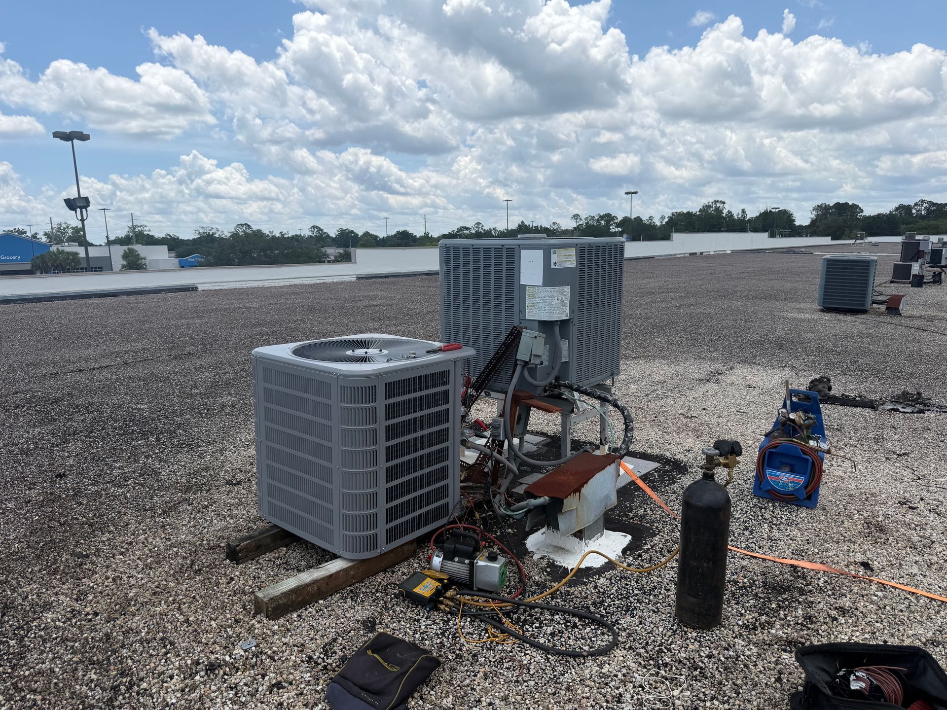 Rooftop HVAC units and maintenance tools on a gravel-covered flat roof under a cloudy sky