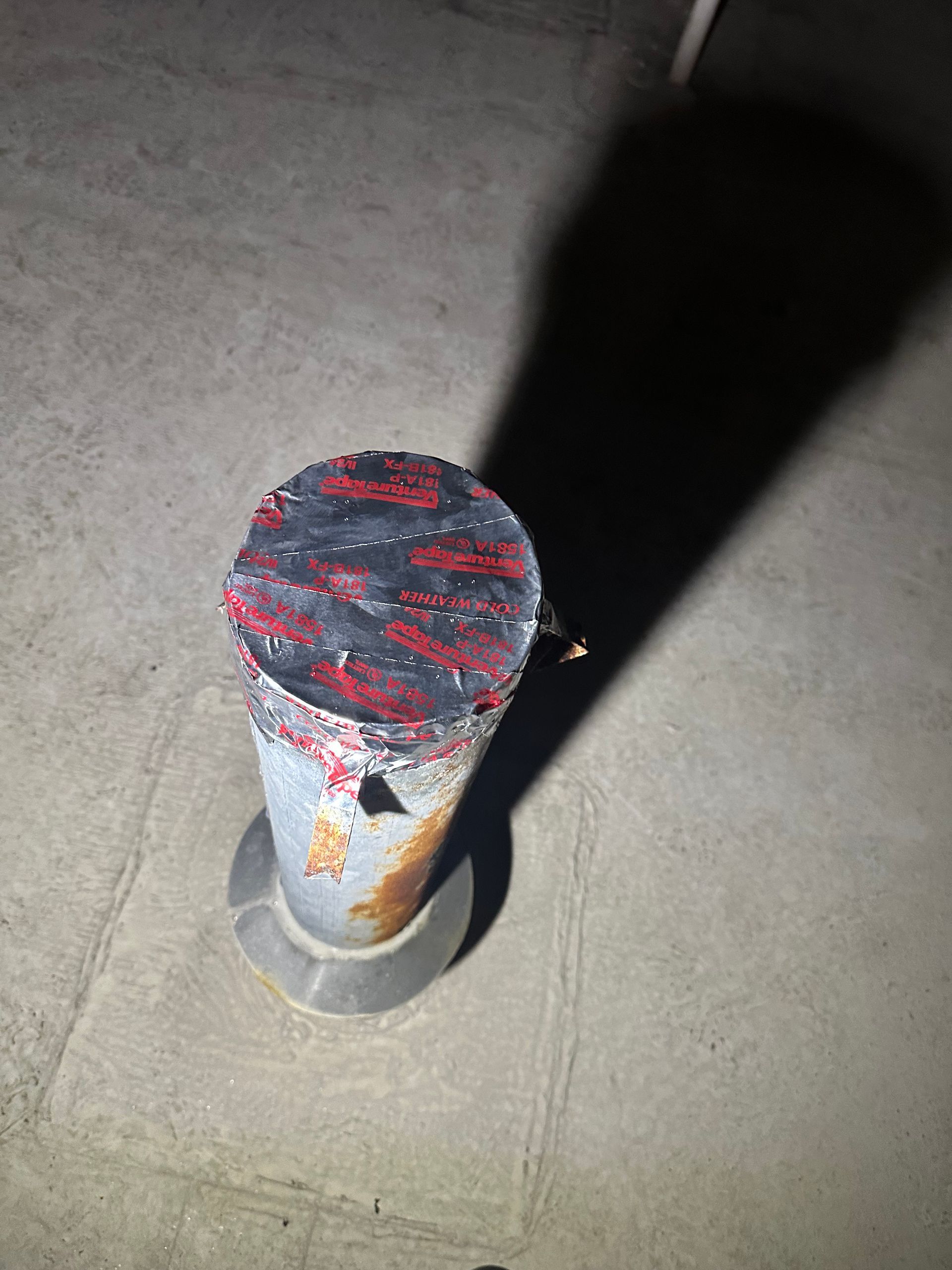 Capped metal post with red paint and black shadow on a concrete floor