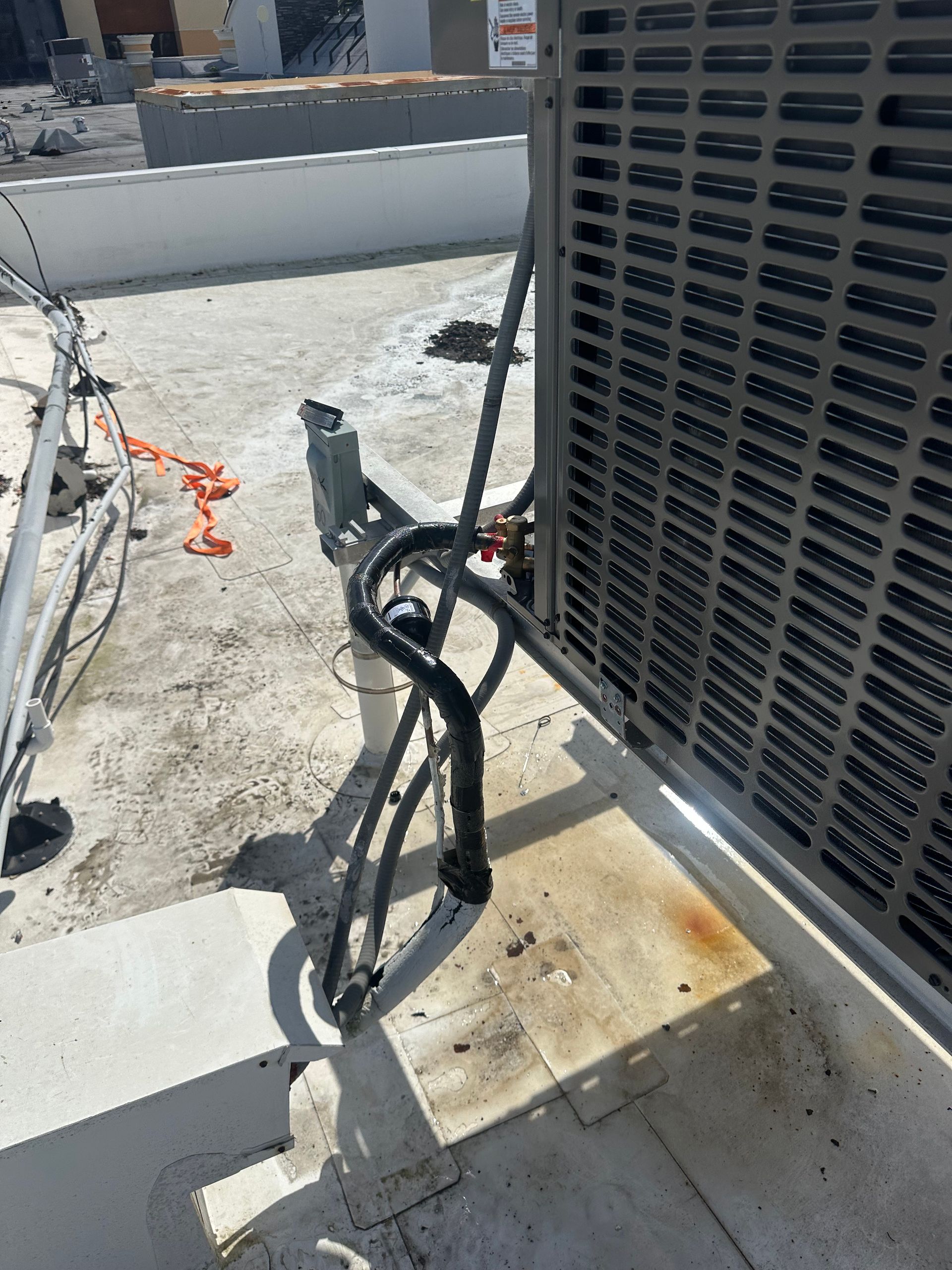 Black utility equipment and cables beside a rooftop HVAC unit on a concrete surface.